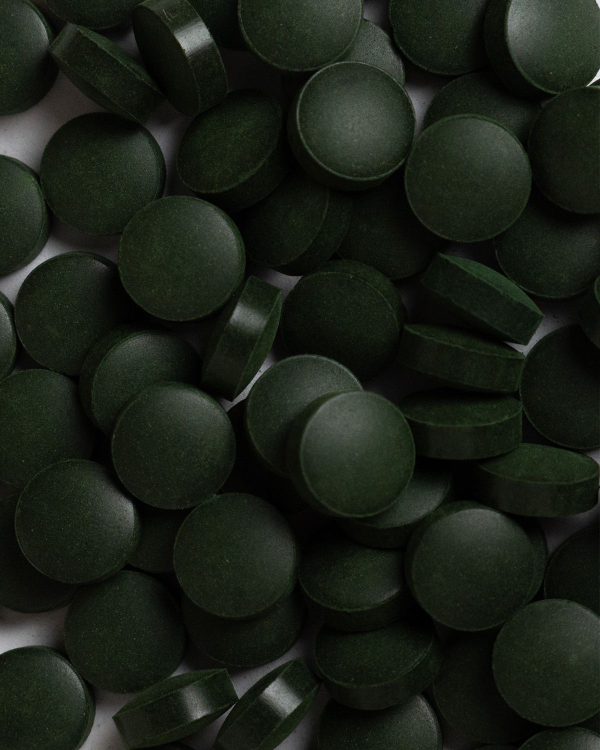 Nahaufnahme von vielen dunkelgrünen, runden Tabletten. Tabletten liegen dicht aneinander.