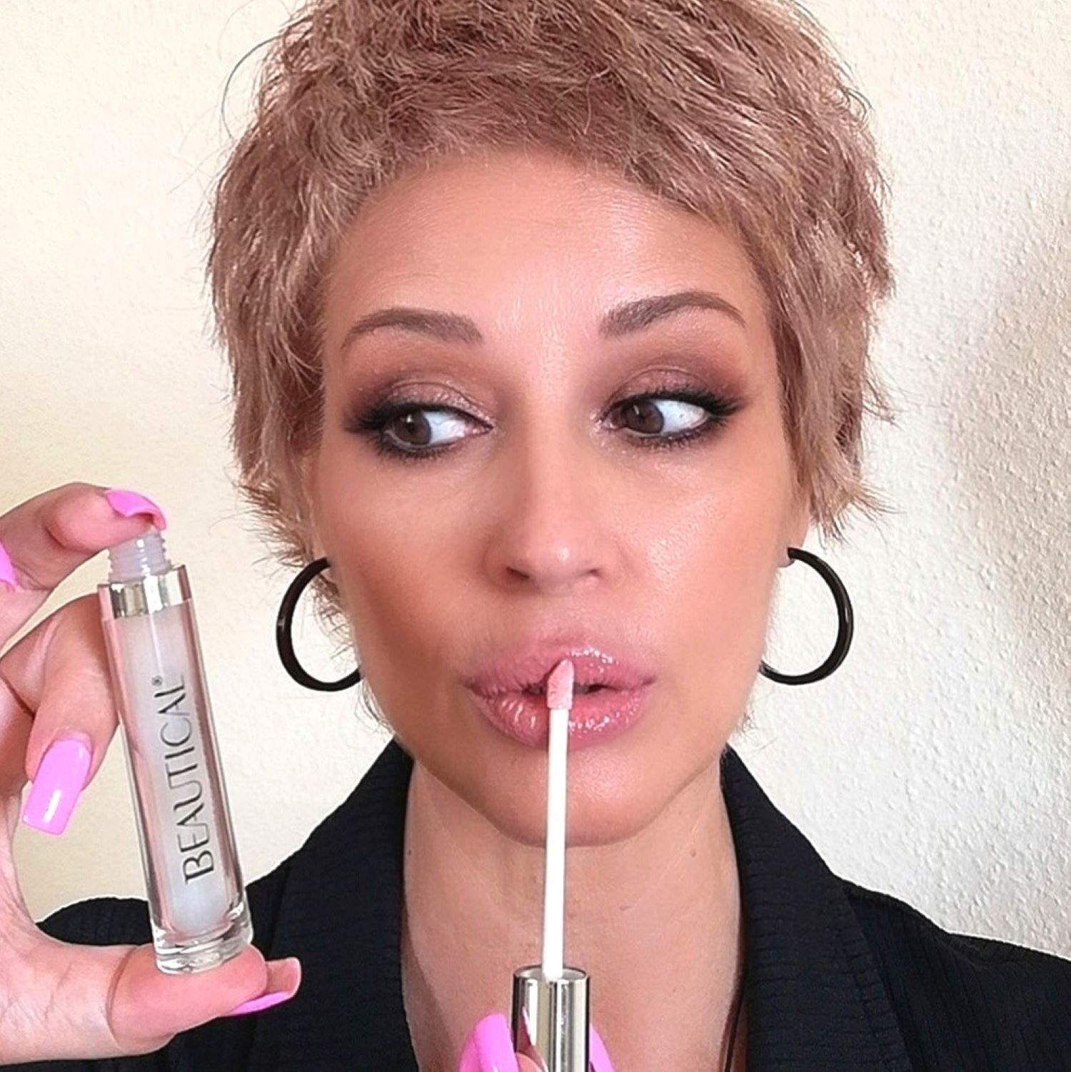 Frau hält BEAUTICAL Instant Lip Plumper. Sie trägt Lippenstift und blickt zur Seite. Schwarze Ohrringe.