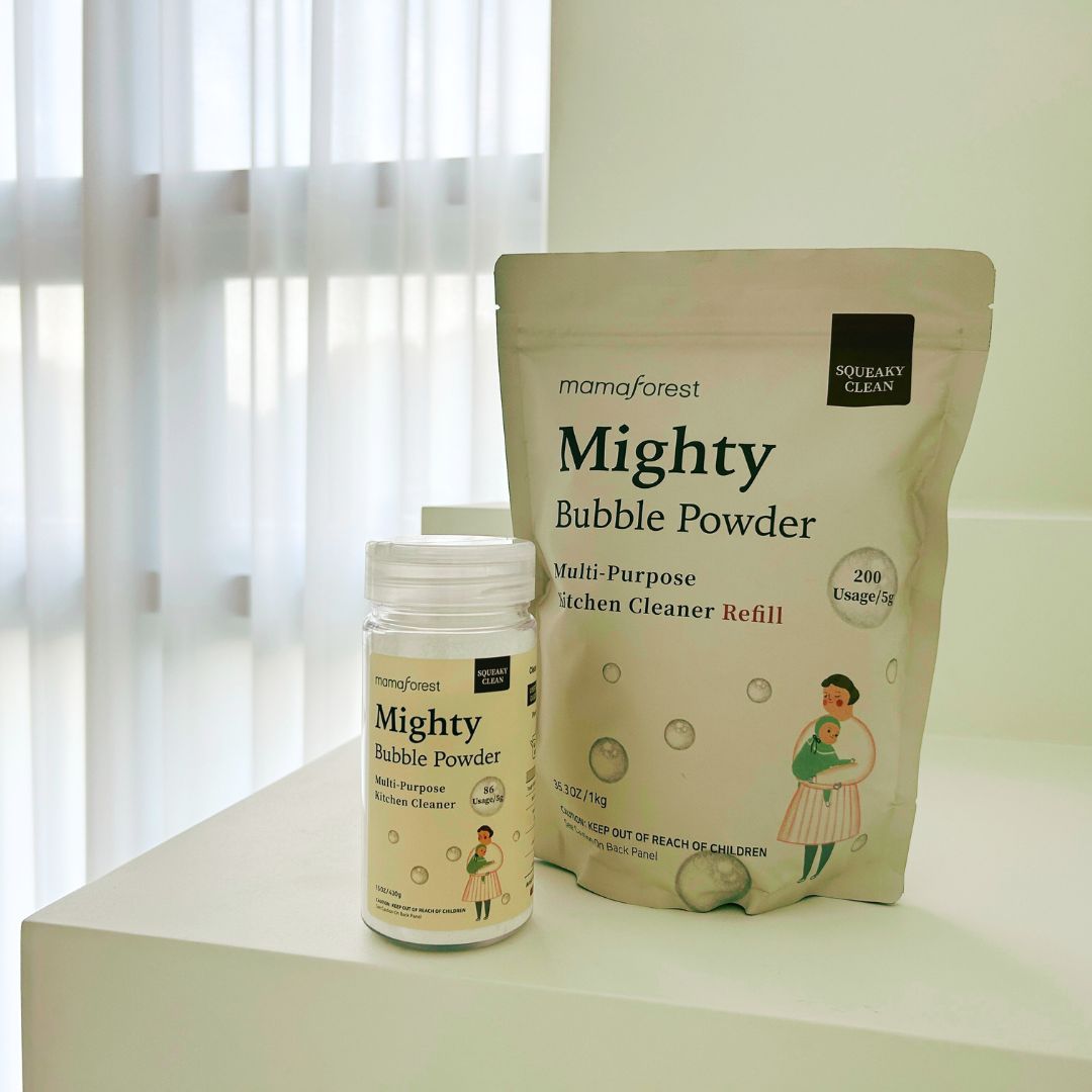 Beutel und Flasche "Mighty Bubble Powder". Aufschrift: "Multi-Purpose Kitchen Cleaner Refill". Flasche mit Etikett. Hintergrund: Fenster und Vorhang.