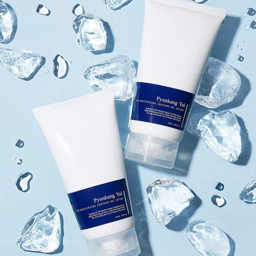Zwei weiße Tuben mit blauem Etikett. Aufschrift: PYUNKANG YUL ATO Moisturizing Soothing Gel Lotion. Umgeben von Eiswürfeln und Wassertropfen.