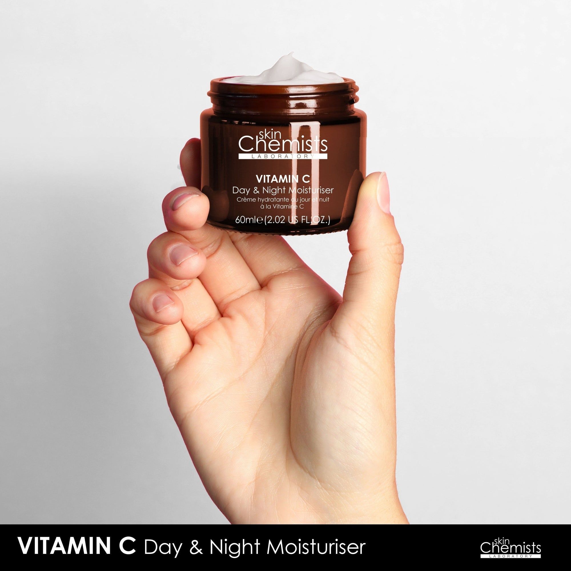 Hand hält braune Glasdose mit schwarzem Deckel. Aufschrift: Vitamin C Day & Night Moisturiser. Marke: skinChemists.