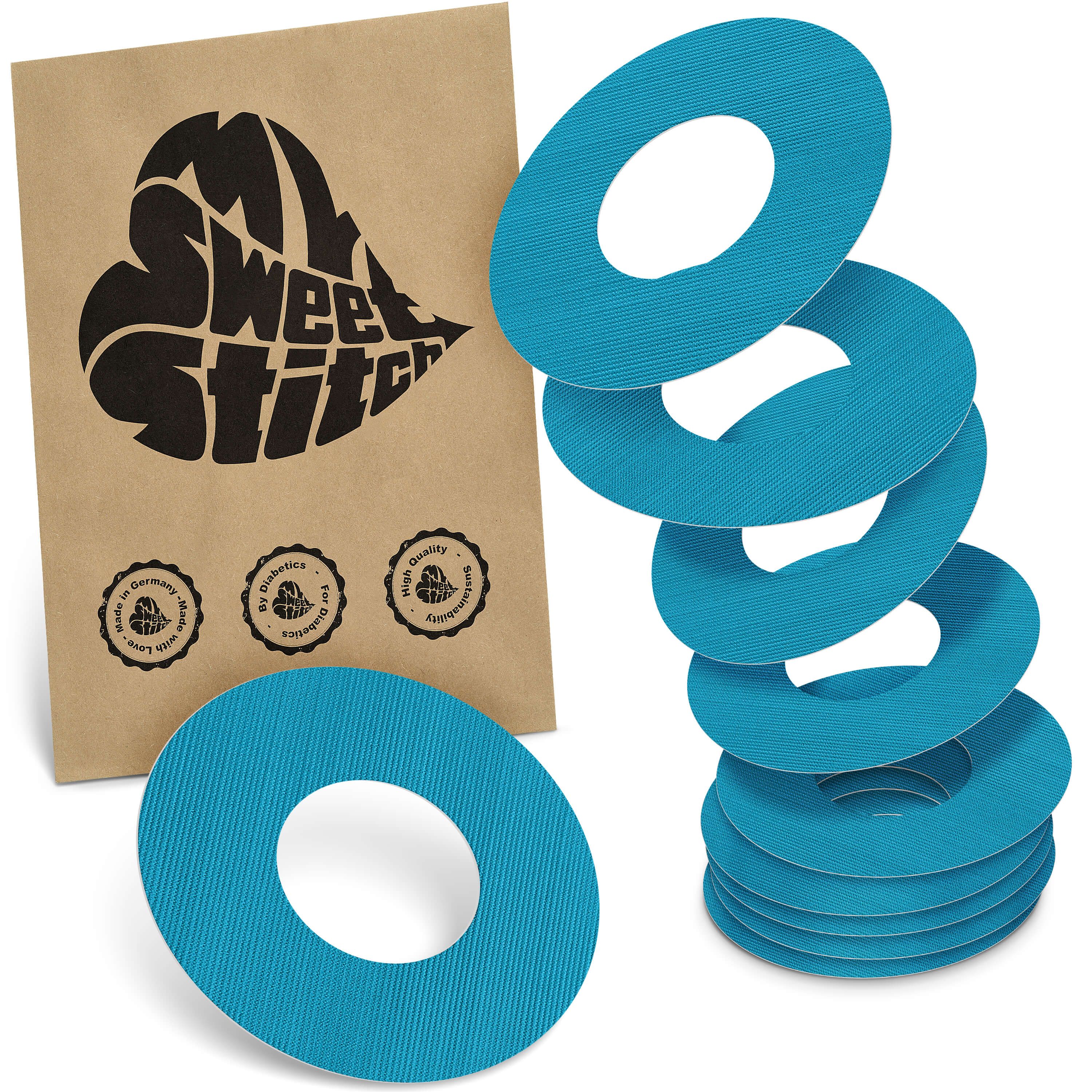 Blau-türkise, ringförmige Pflaster mit zentraler Öffnung. Neben einer Papiertüte mit Logo und Siegeln. Mehrere Ringe gestapelt.