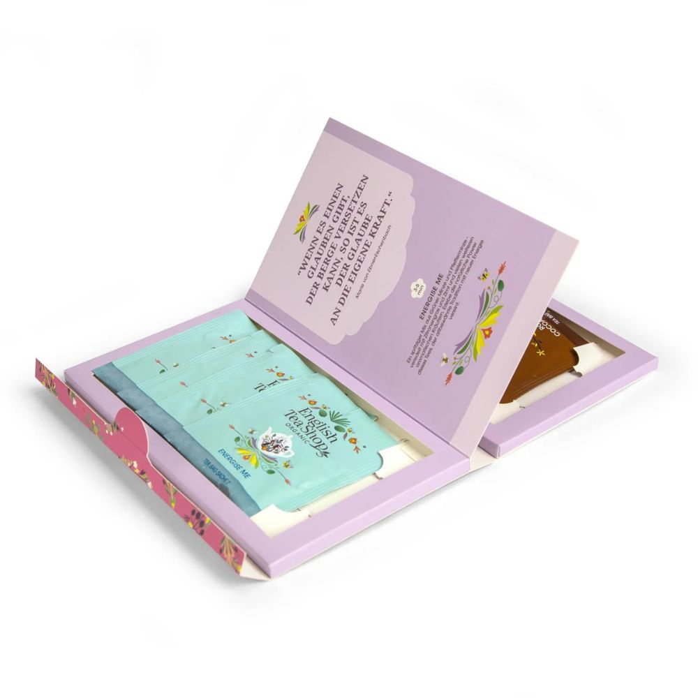 Geöffnete Geschenkbox. Innenliegende Teebeutel in hellblau und braun. Zitat auf der Innenseite des Deckels. Rosa Umrandung.