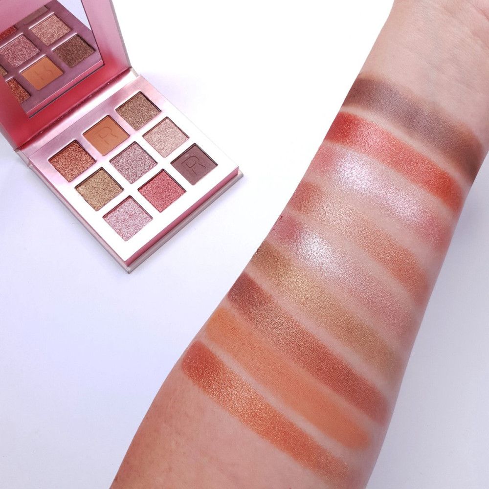 Arm mit Swatches von Lidschattenfarben. Palette im Hintergrund. Verschiedene Braun- und Rosatöne.