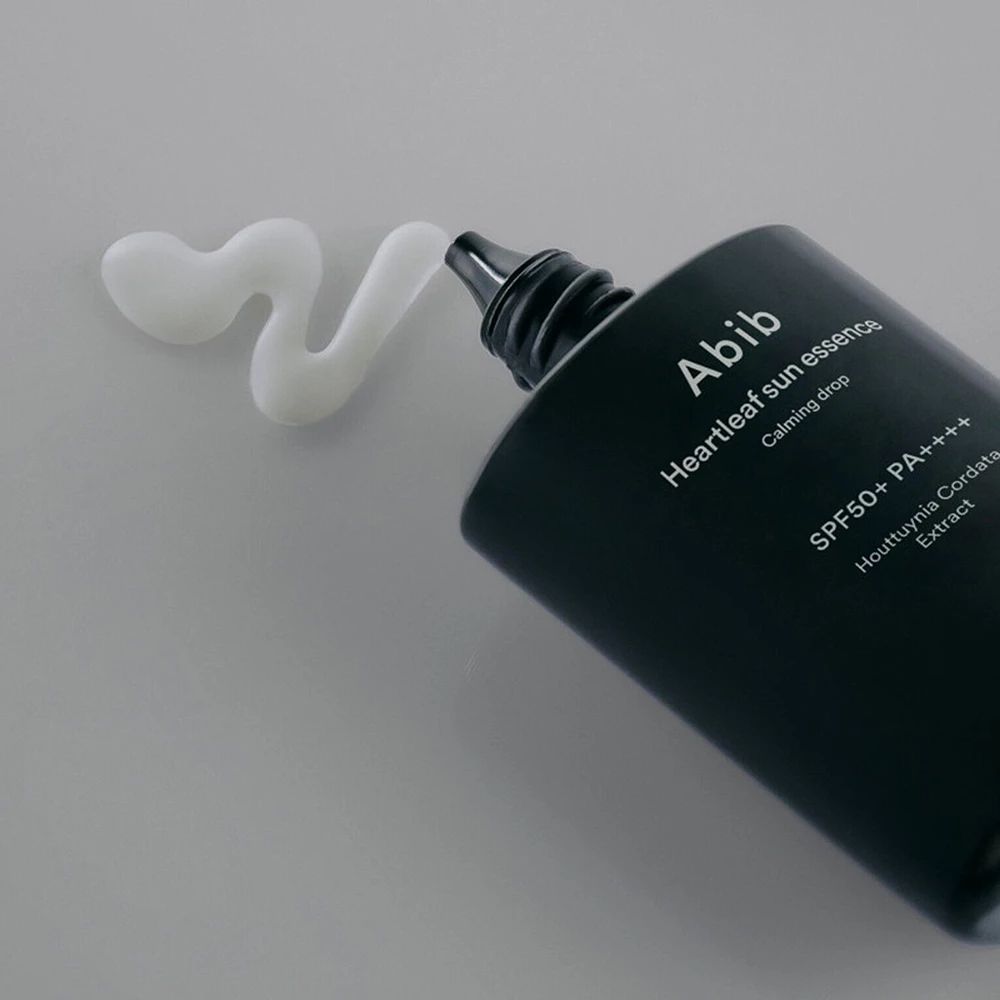 Nahaufnahme einer schwarzen Flasche, aus der eine weiße Creme austritt. Aufschrift: Abib Heartleaf Sun Essence.