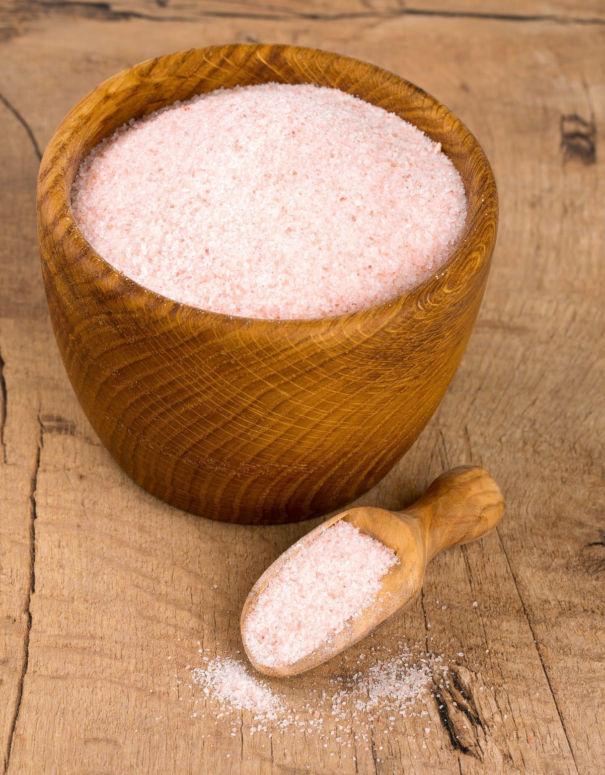 Holzschale mit rosa Salz, daneben ein kleiner Holzlöffel. Auf rustikalem Holzuntergrund.