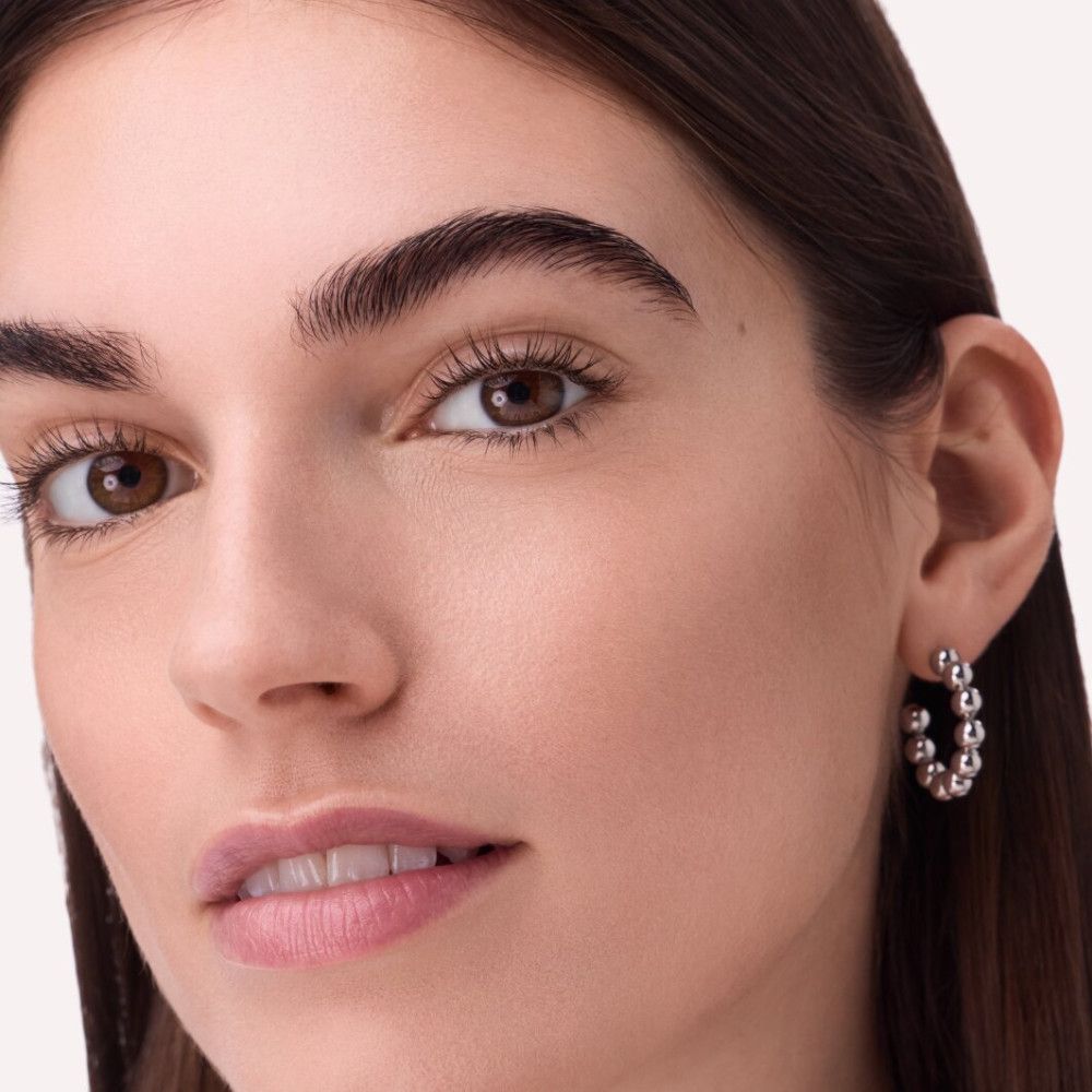 Nahaufnahme einer Frau mit hellbraunen Augen und Ohrringen. Die Ohrringe sind silberfarbene Kugel-Creolen.