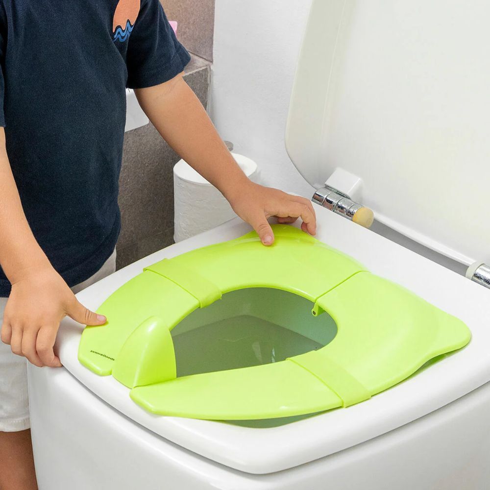 Grüner Toilettensitz für Kinder auf einer Toilette. Kind legt den Sitz auf. Marke InnovaGoods.