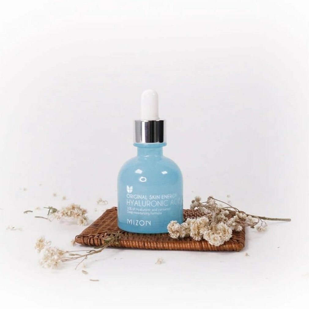 Hellblaue Flasche mit silbernem Deckel und Pipette auf einem kleinen Tablett mit Trockenblumen. Marke: Mizon.