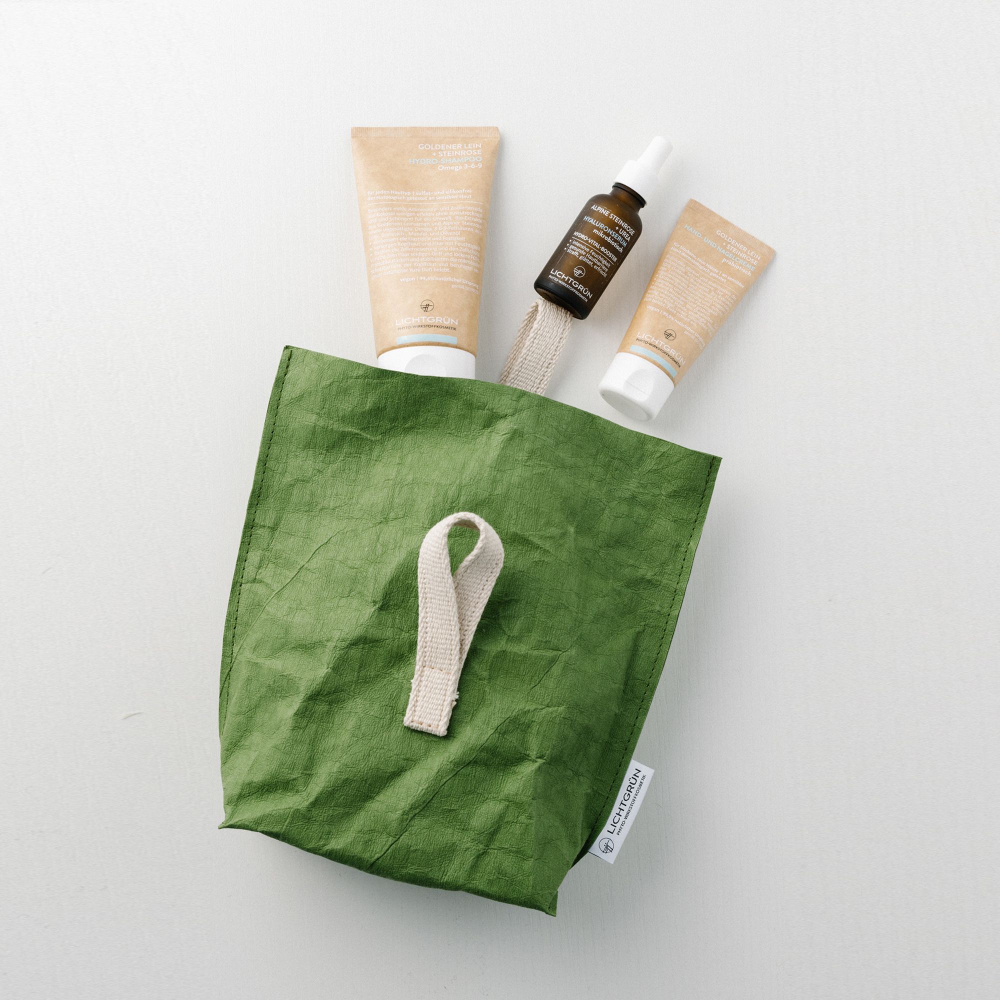 Geschenkset mit Kosmetikprodukten in einer grünen Tasche. Enthält Tuben, eine Flasche mit Pipette und eine Tasche mit Henkel.