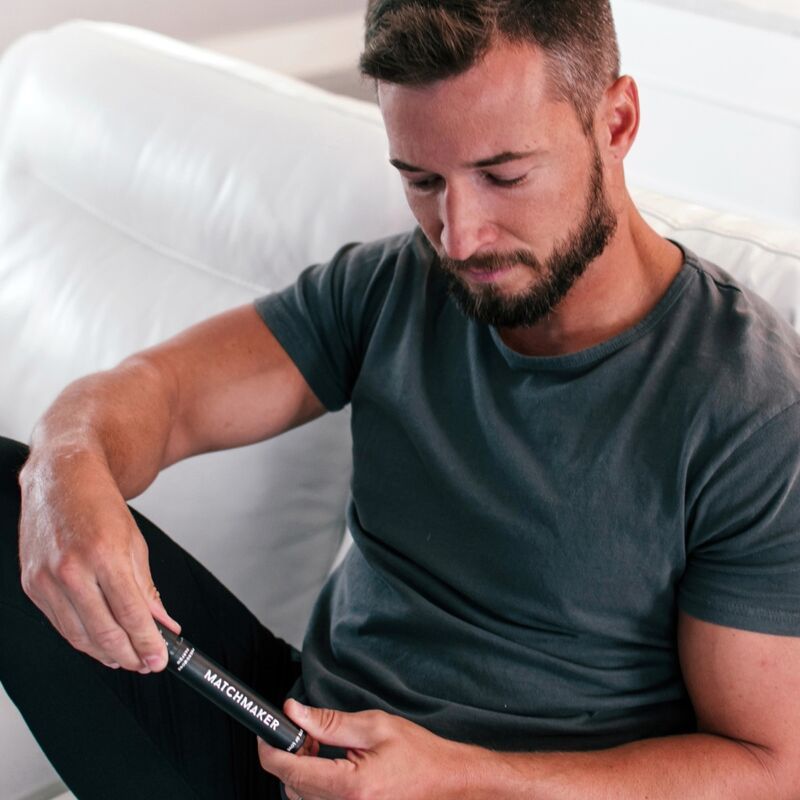 Mann hält die Verpackung des Parfüms. Schwarze zylindrische Verpackung mit weißem Schriftzug MATCHMAKER.