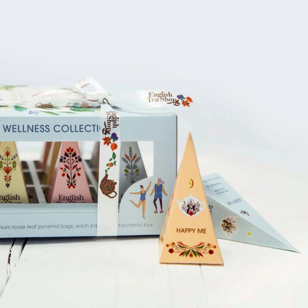 Geschenkbox mit Teebeuteln in pyramidenförmiger Verpackung. Aufschrift: English Tea Shop Wellness Kollektion. Mit Schleife.