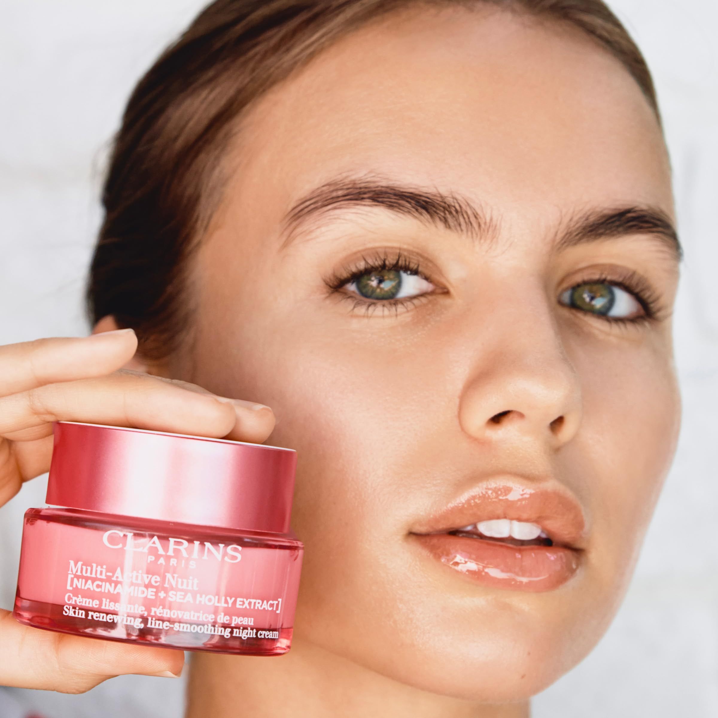 Frau hält rosa Cremetiegel. Aufschrift: CLARINS PARIS, Multi-Active Nuit. Text: Skin renewing, line-smoothing night cream.