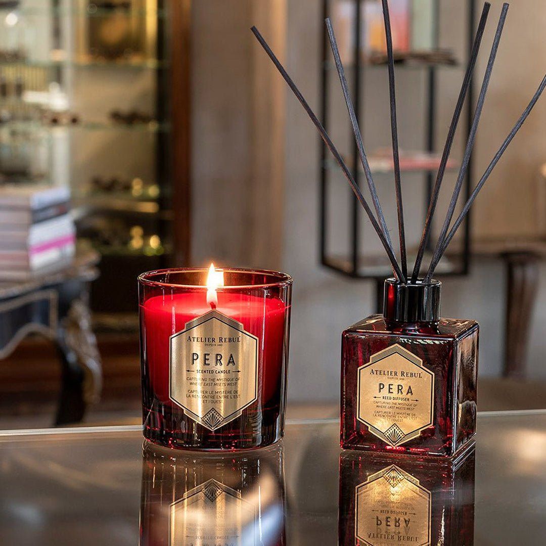Rote Kerze und Diffusor mit schwarzen Stäbchen. Beide mit Etikett "Pera" von Atelier Rebul. Kerze brennt.