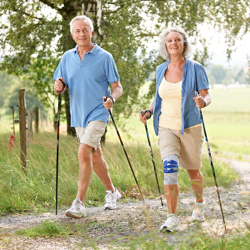 Älteres Paar beim Spaziergang im Freien. Frau mit Kniebandage. Wanderstöcke.