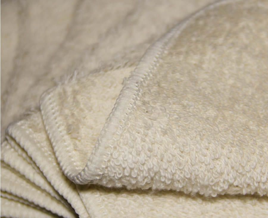 Nahaufnahme eines cremefarbenen Frottee-Waschlappens. Sichtbare Naht am Rand.