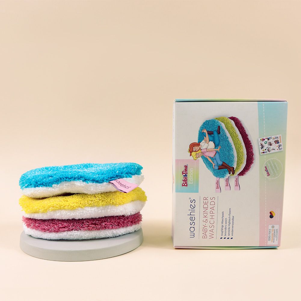 Vier farbige Waschpads gestapelt auf einem grauen Untersetzer. Daneben steht eine Verpackung mit dem Logo "waschies Bibi & Tina Edition".