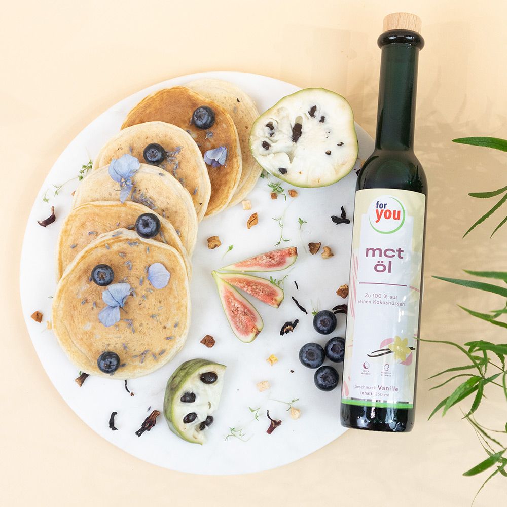 Glasflasche mit weißem Etikett neben Pfannkuchen, Obst und Blaubeeren. Aufschrift: for you mct öl.