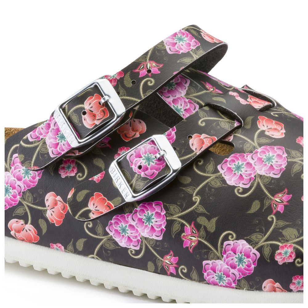 Detailansicht der Pantolette. Schwarzer Hintergrund, rosa und rote Blüten. Zwei verstellbare Riemen mit Schnallen. Birkenstock-Logo.