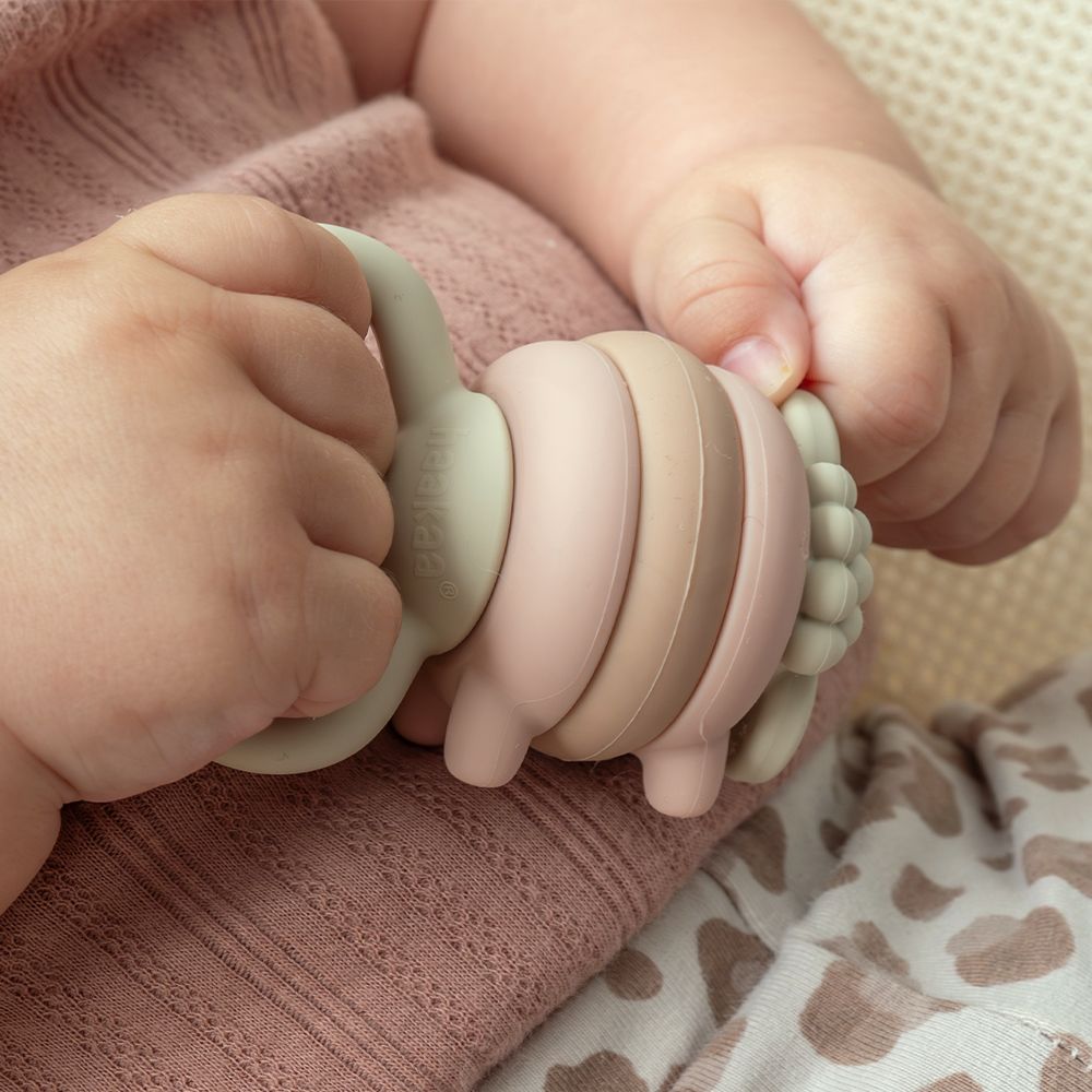 Ein Baby hält einen bunten Beißring in Schaf-Form.