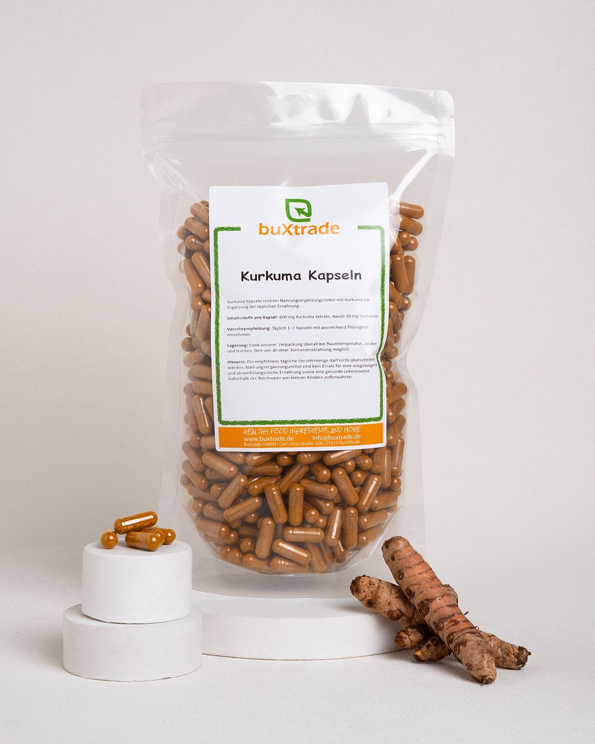 Verpackung mit Kurkuma-Kapseln, daneben Kurkumawurzeln und Kapseln.