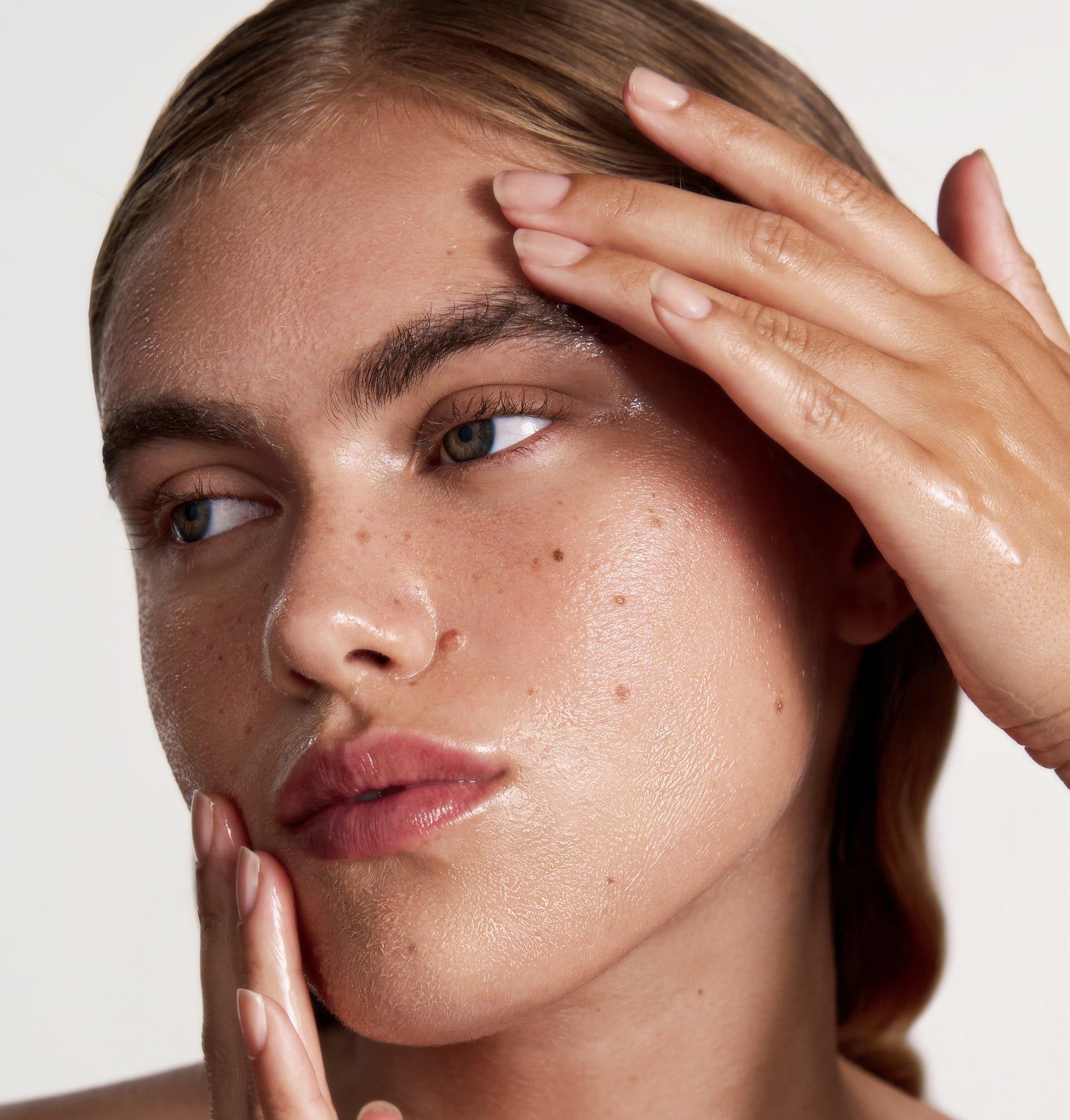 Gesicht einer Frau mit Öl auf der Haut. Hände berühren das Gesicht. Haut glänzt.