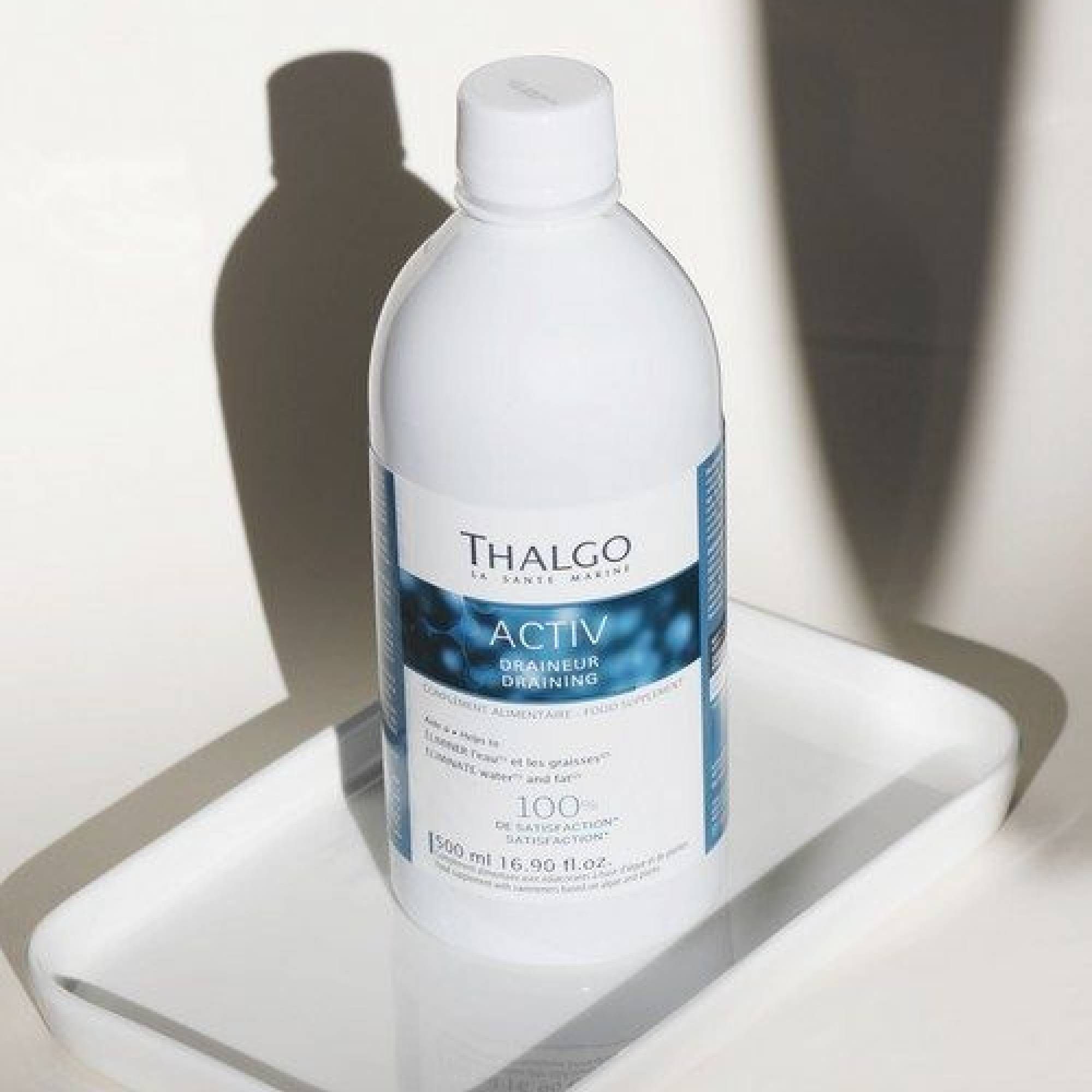 Weiße Flasche mit blauem Etikett. Text: ACTIV Draineur, THALGO. Auf weißem Tablett. Flaschenverschluss.