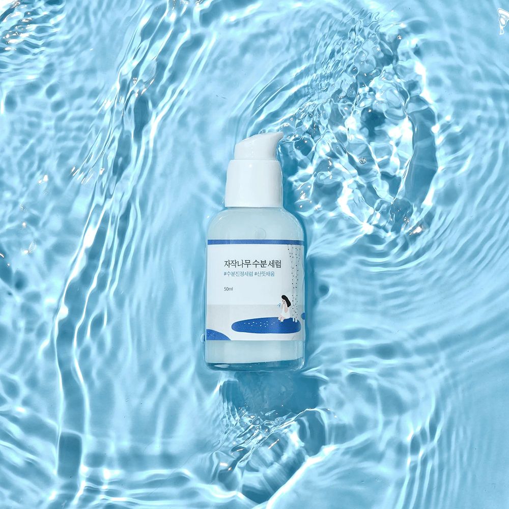 Round Lab Birch Juice Serum, 50ml, in Pumpspender inmitten von Wasserwellen.