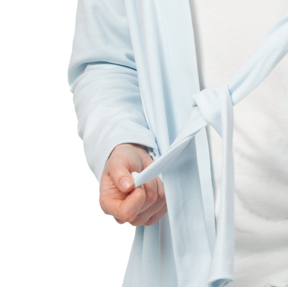 Nahaufnahme einer Hand, die den Bindegürtel eines hellblauen Morgenmantels knotet.