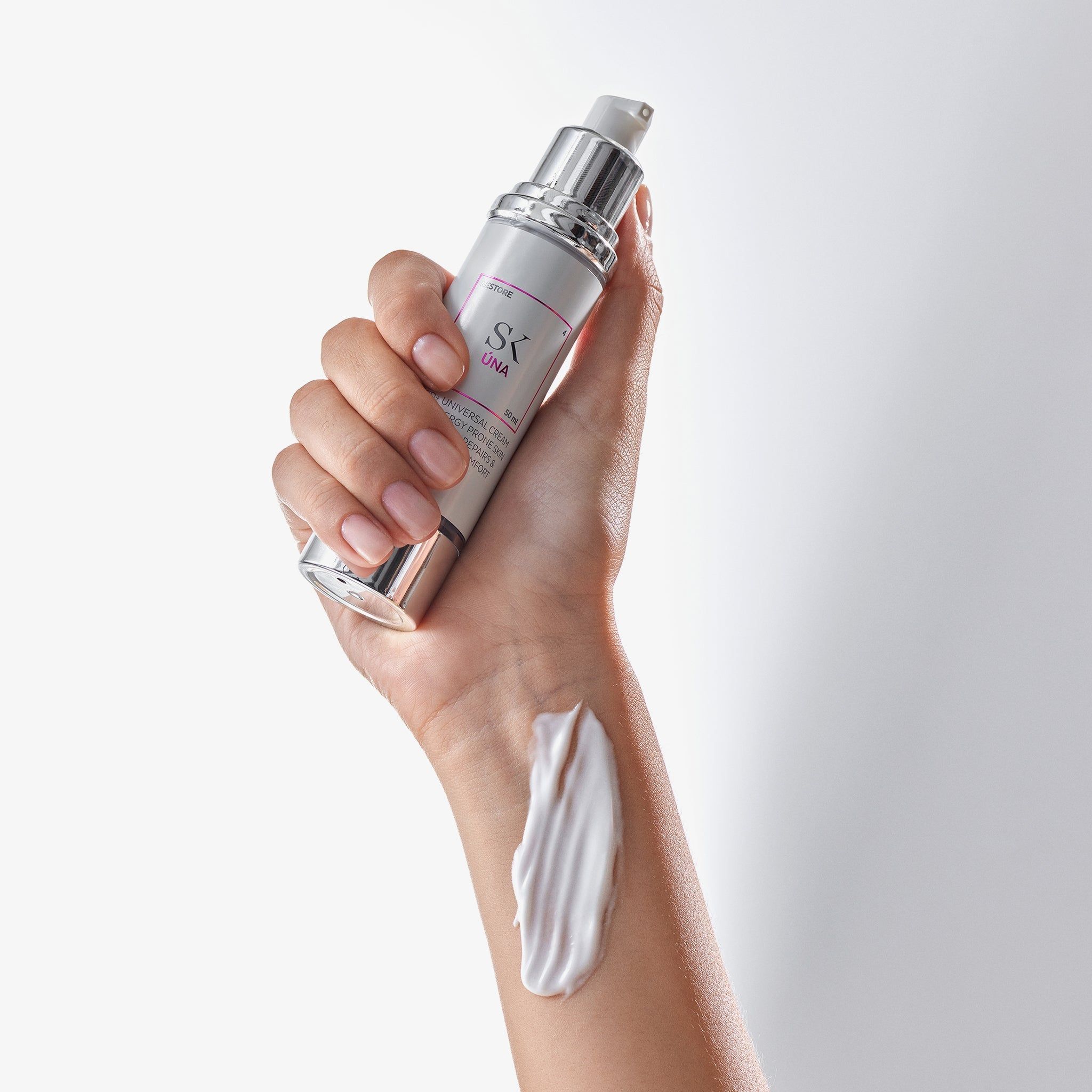 Hand hält Creme-Spender. Auf dem Handrücken Creme-Klecks. Aufschrift: SK Úna. Creme weiß.