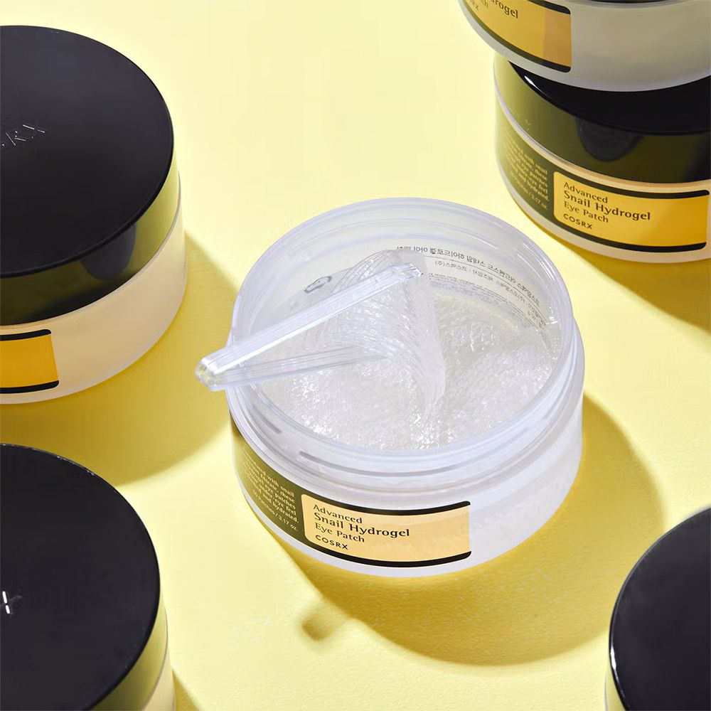Offener Behälter mit Hydrogel-Augenpads und Spatel auf gelbem Hintergrund.