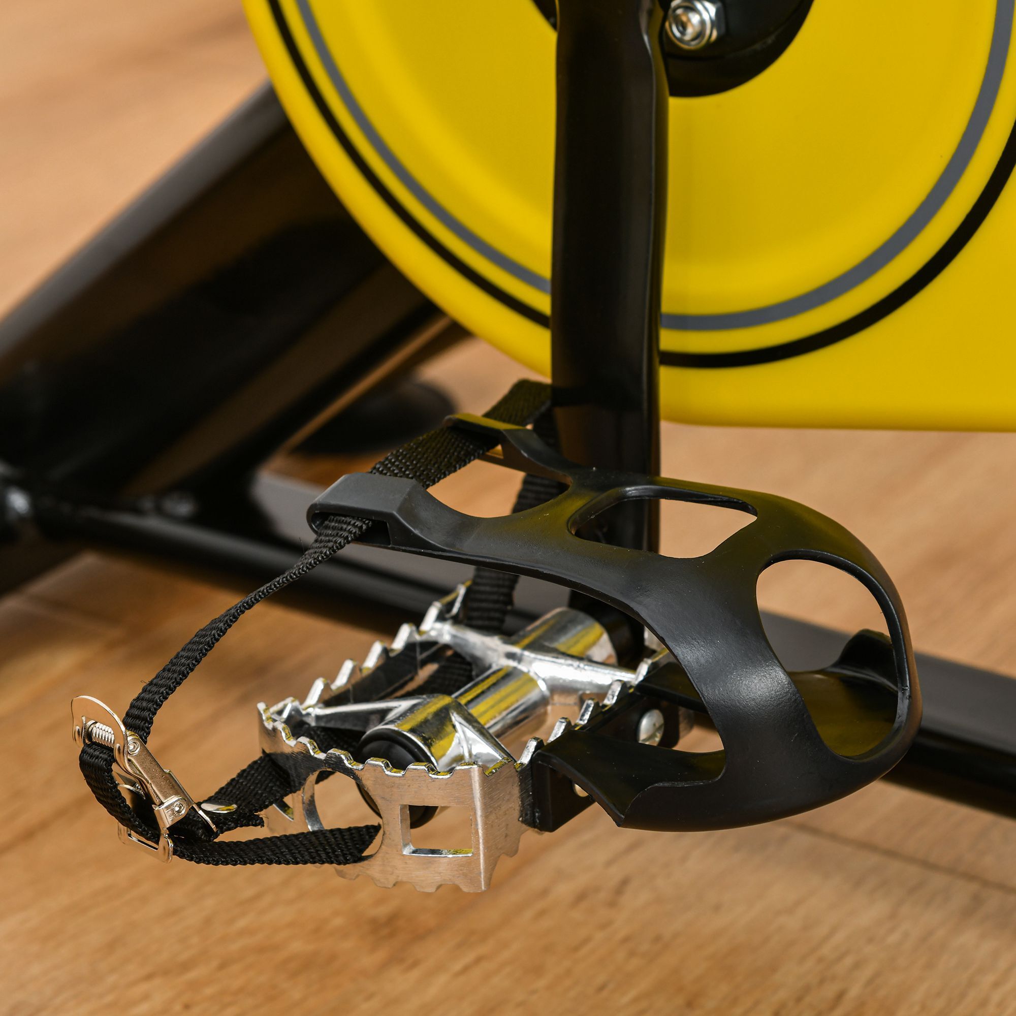 Fahrradpedal mit schwarzem Riemen. Schwarzer Kunststoff, silbernes Metall. Gelbes Rad im Hintergrund.