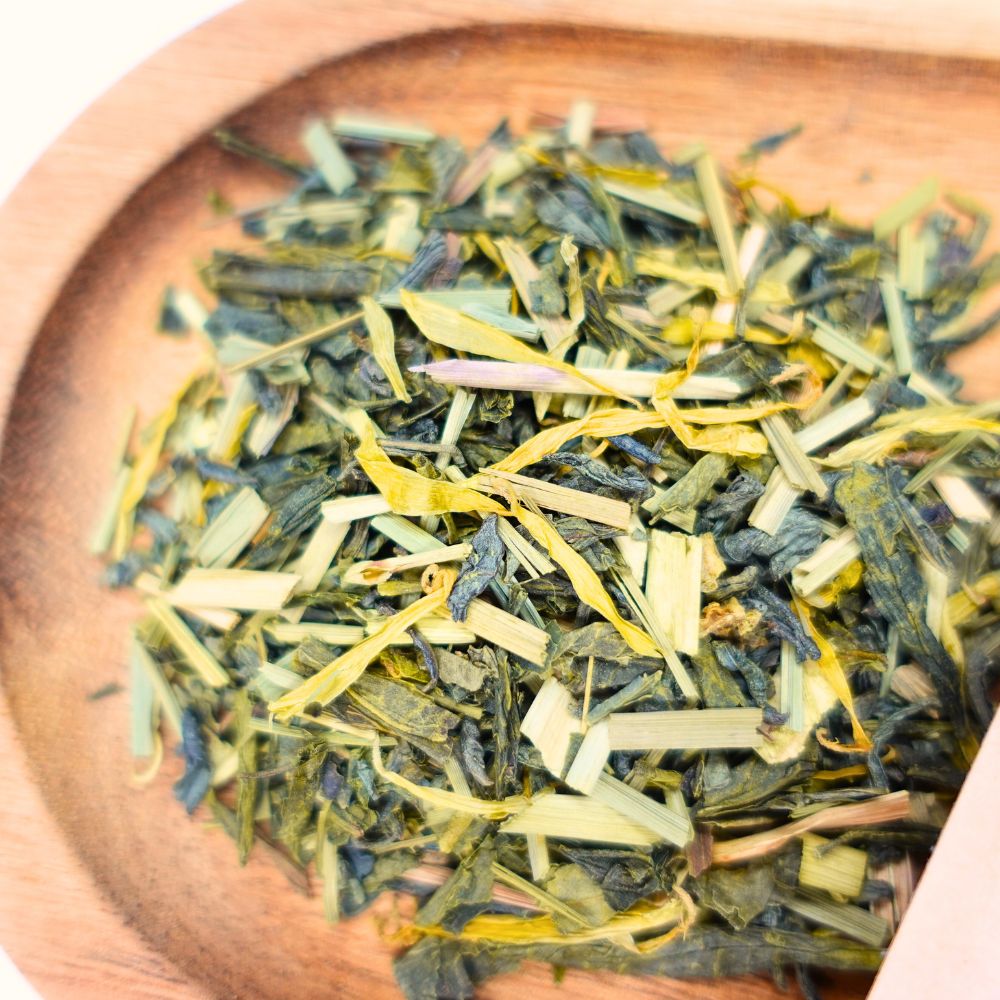 Grüner Tee mit Zitronengras in einer Holzschale. Die Mischung enthält grüne Teeblätter und gelbes Zitronengras.