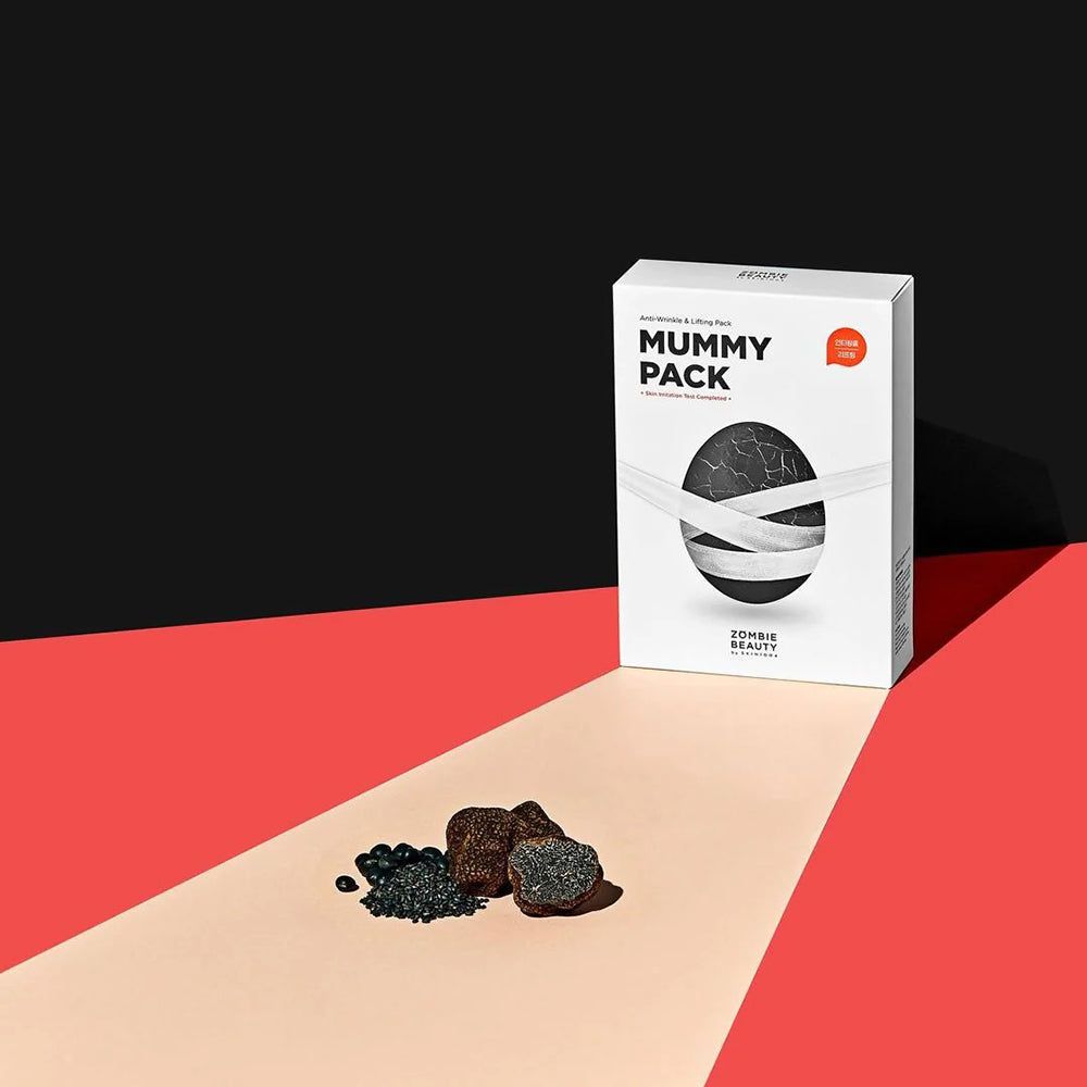 Weiße Verpackung mit "Mummy Pack"-Schriftzug. Schwarze Maske mit weißen Bändern. Schwarze und rote Akzente. Marke: ZOMBIE BEAUTY.