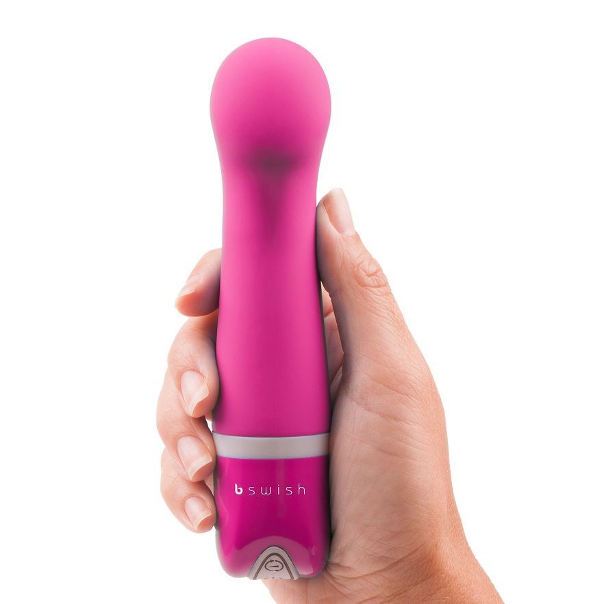 Hand hält pinken Silikonvibrator mit weißem Ring und silbernem Bedienelement.