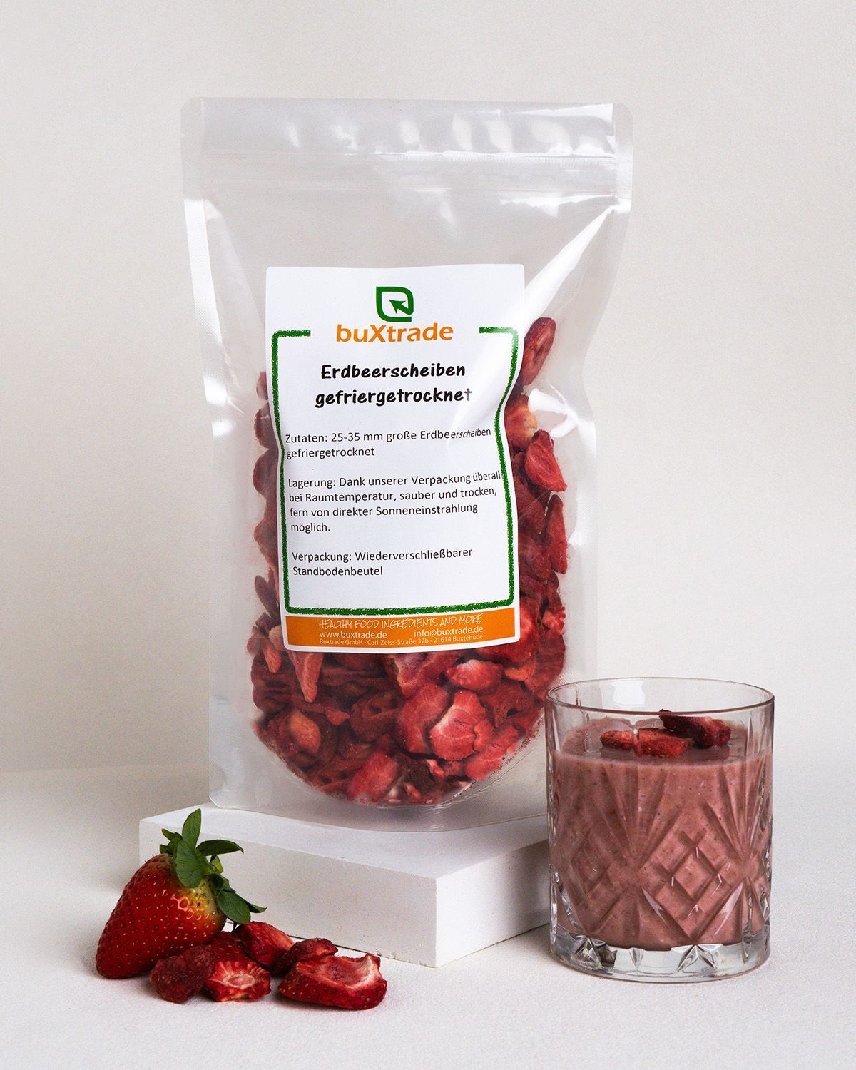 Transparente Beutel mit gefriergetrockneten Erdbeerscheiben. Aufdruck mit Produktname. Daneben ein Glas Smoothie und frische Erdbeeren.