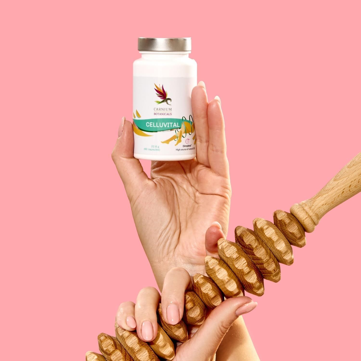 Hand hält Flasche CELLUVITAL und Massagegerät. Rosa Hintergrund.