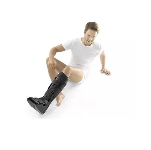 Mann sitzt mit Air Walker am Bein. Schwarzer Stiefel, Klettverschlüsse. Weißes T-Shirt, Unterhose.