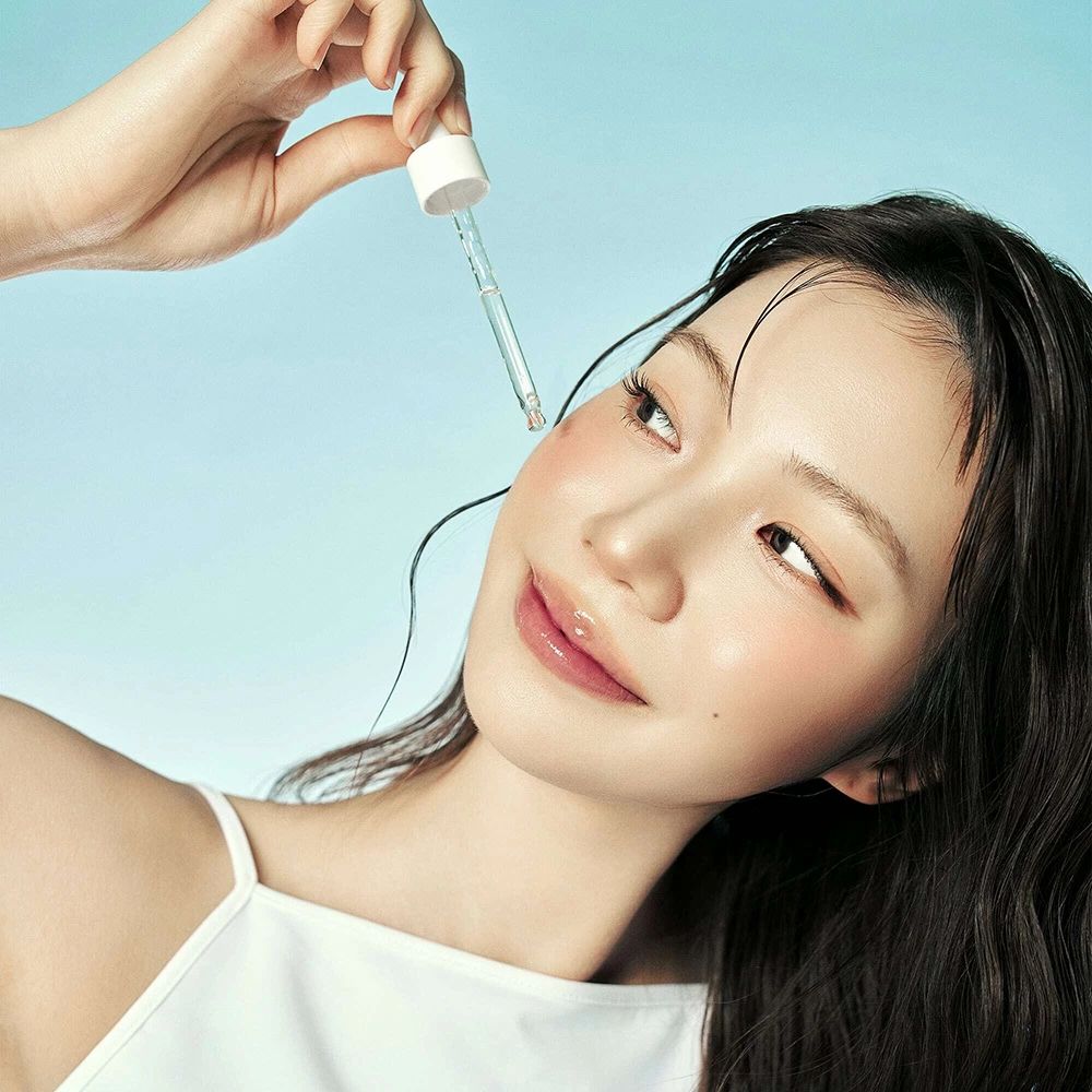 Frau mit Serum-Applikator. Serum wird auf die Wange aufgetragen. Blauer Hintergrund.