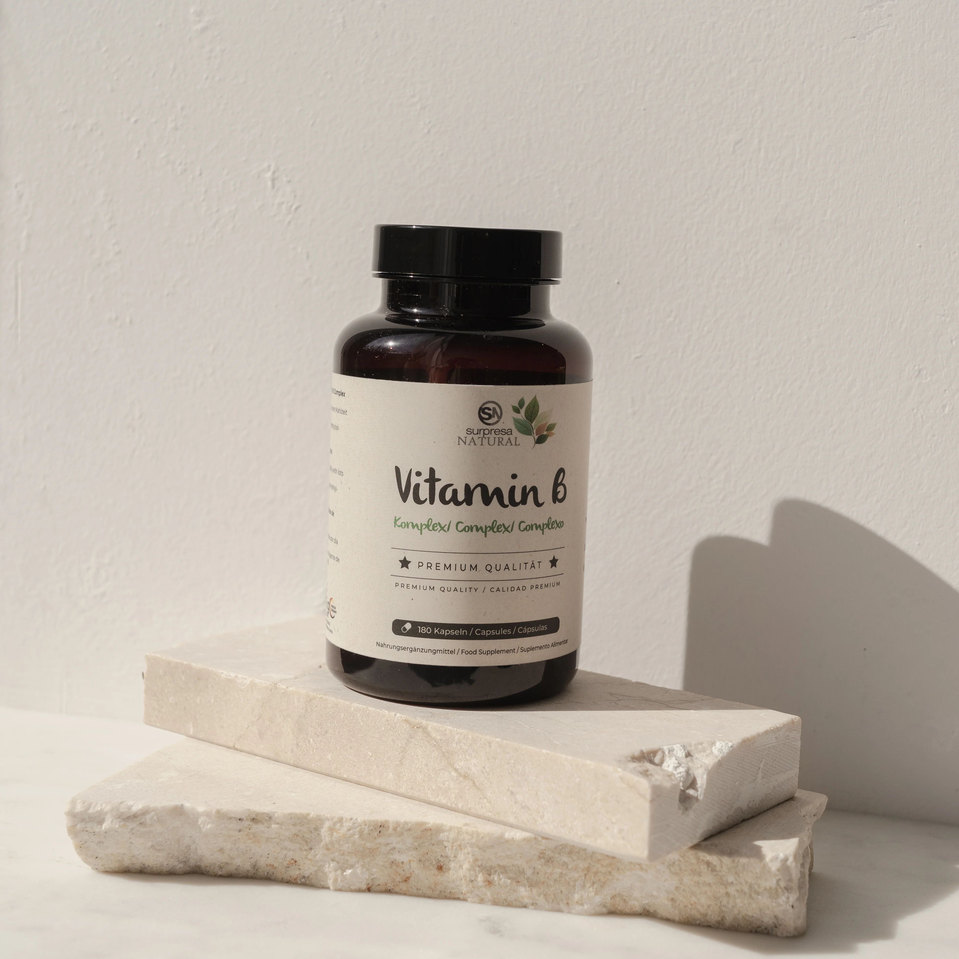 Braune Flasche mit schwarzem Deckel. Etikett mit "Vitamin B" und "Premium Qualität". Steht auf zwei hellen Steinblöcken.