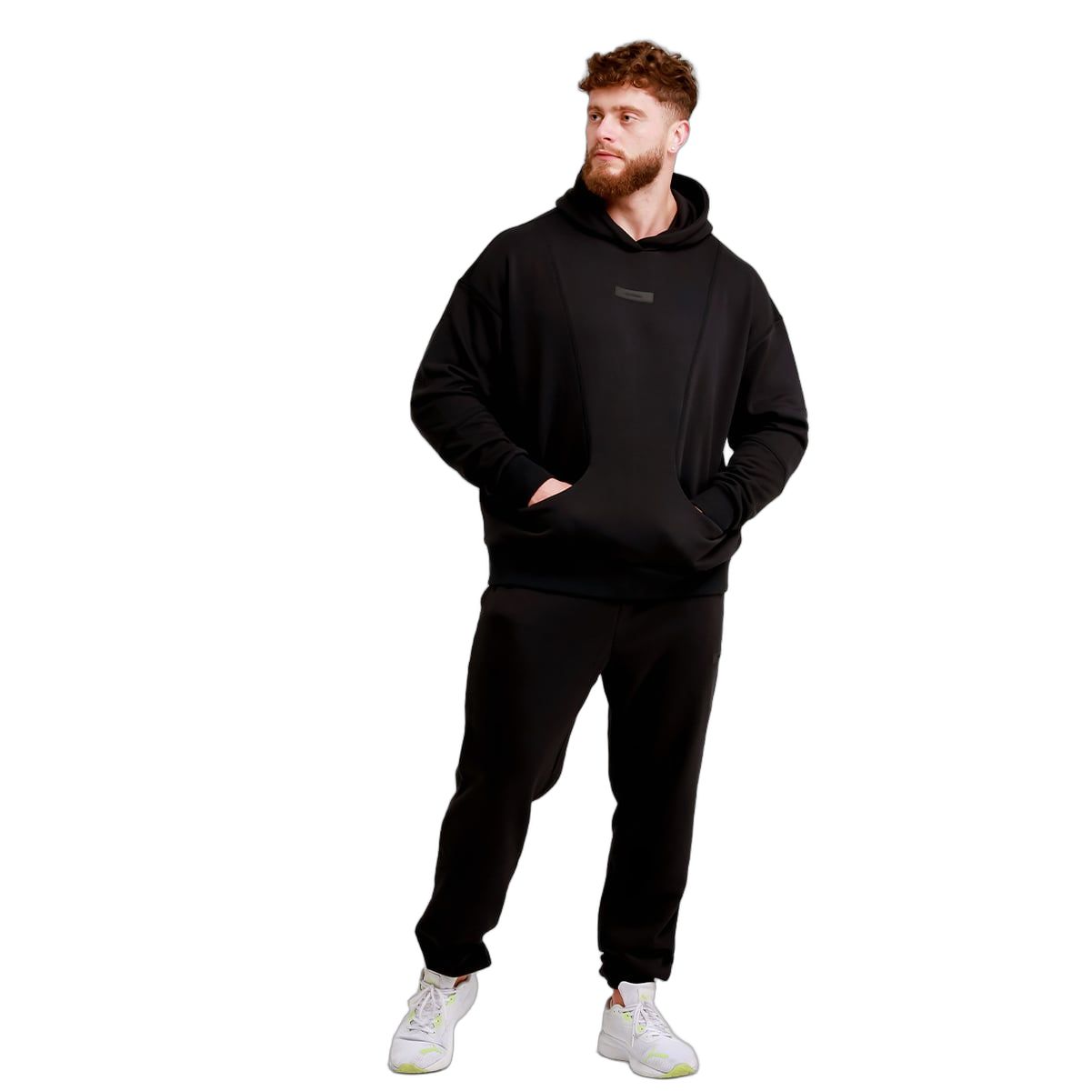 Mann in schwarzer Jogginghose und Kapuzenpullover, Hände in den Hosentaschen.