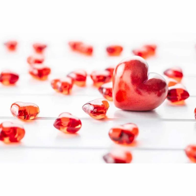 Rote, herzförmige Gelees auf weißem Holzgrund. Ein großes Herz im Fokus.