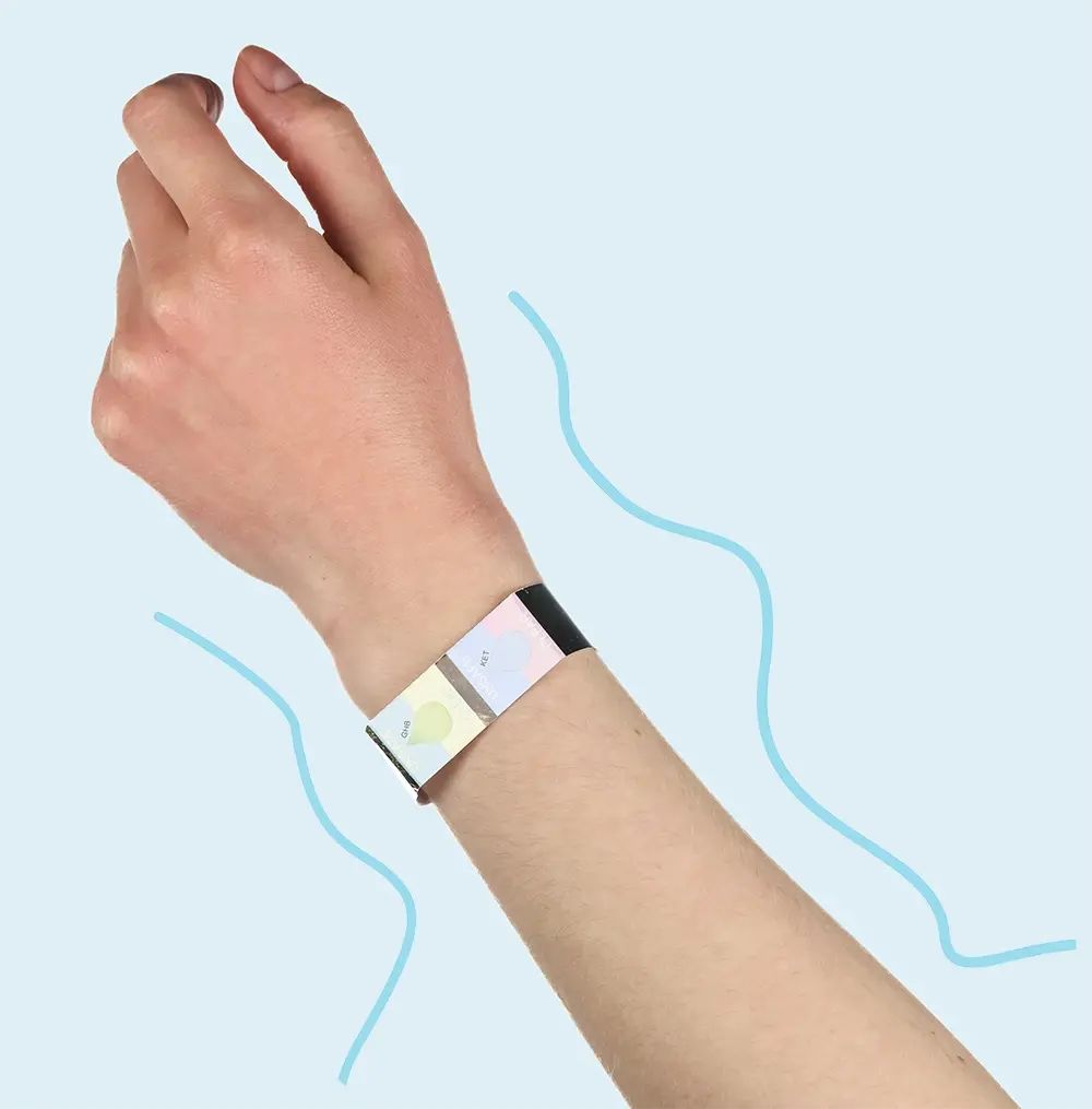 Hand mit Armband am Handgelenk. Das Armband hat mehrere farbige Testfelder. Blaue Linien im Hintergrund.