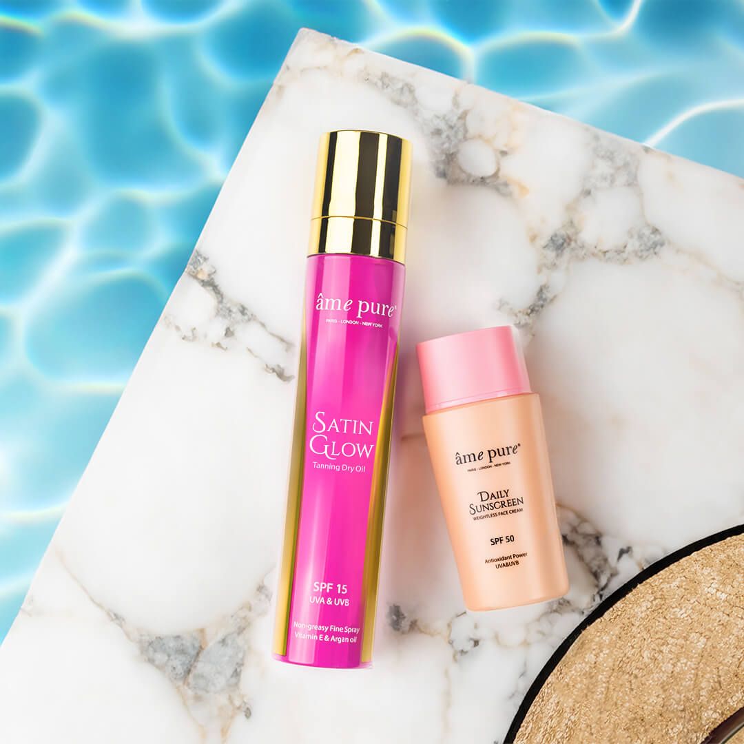Sonnenschutz-Set auf Marmorplatte: Tages-Sonnenschutz SPF 50 und Satin Glow Bräunungsöl.