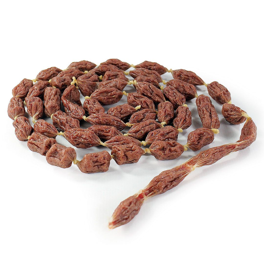 Kette aus getrockneten, braunen Kauartikeln für Hunde. Einzelne Stücke sind durch eine Schnur verbunden. Auf weißem Hintergrund.