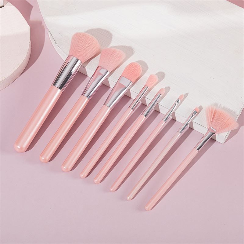 Make-up-Pinsel-Set mit acht rosa Pinseln. Verschiedene Formen und Größen, mit silbernen Metallhülsen und rosa Griffen. Auf rosa Untergrund.