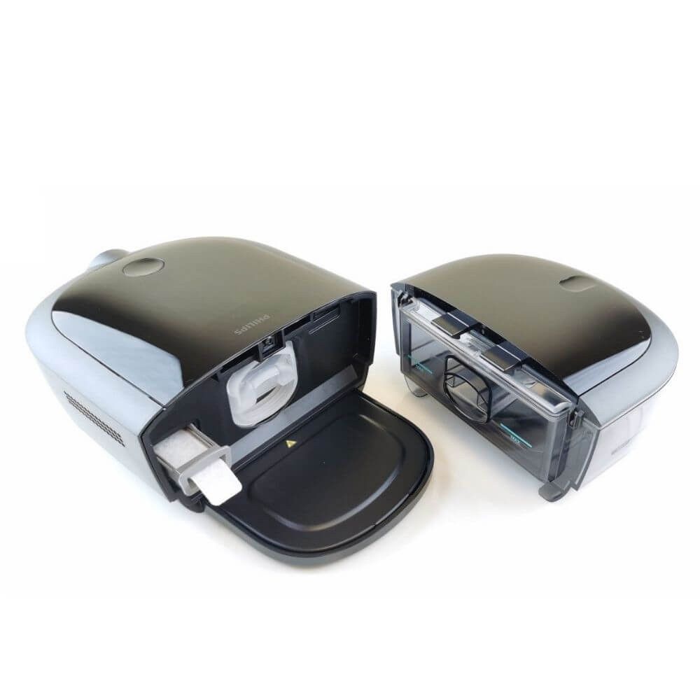 CPAP-Gerät, geöffnet. Wasserkammer und Filterfach sichtbar. Schwarzes Gehäuse, graue Akzente.