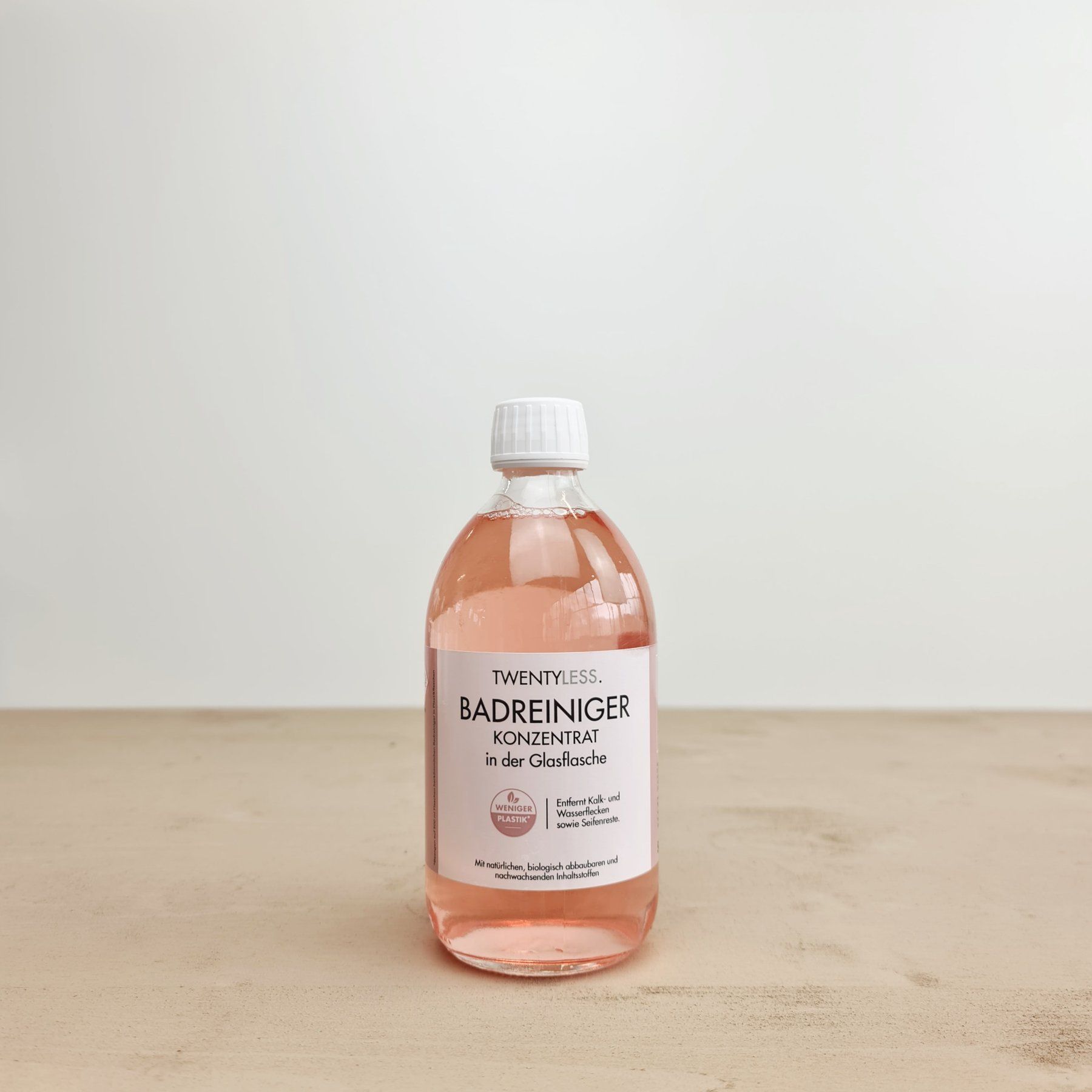 Transparente Flasche mit rosa Flüssigkeit. Aufschrift: TWENTYLESS, Badreiniger Konzentrat in der Glasflasche. Mit Siegel.