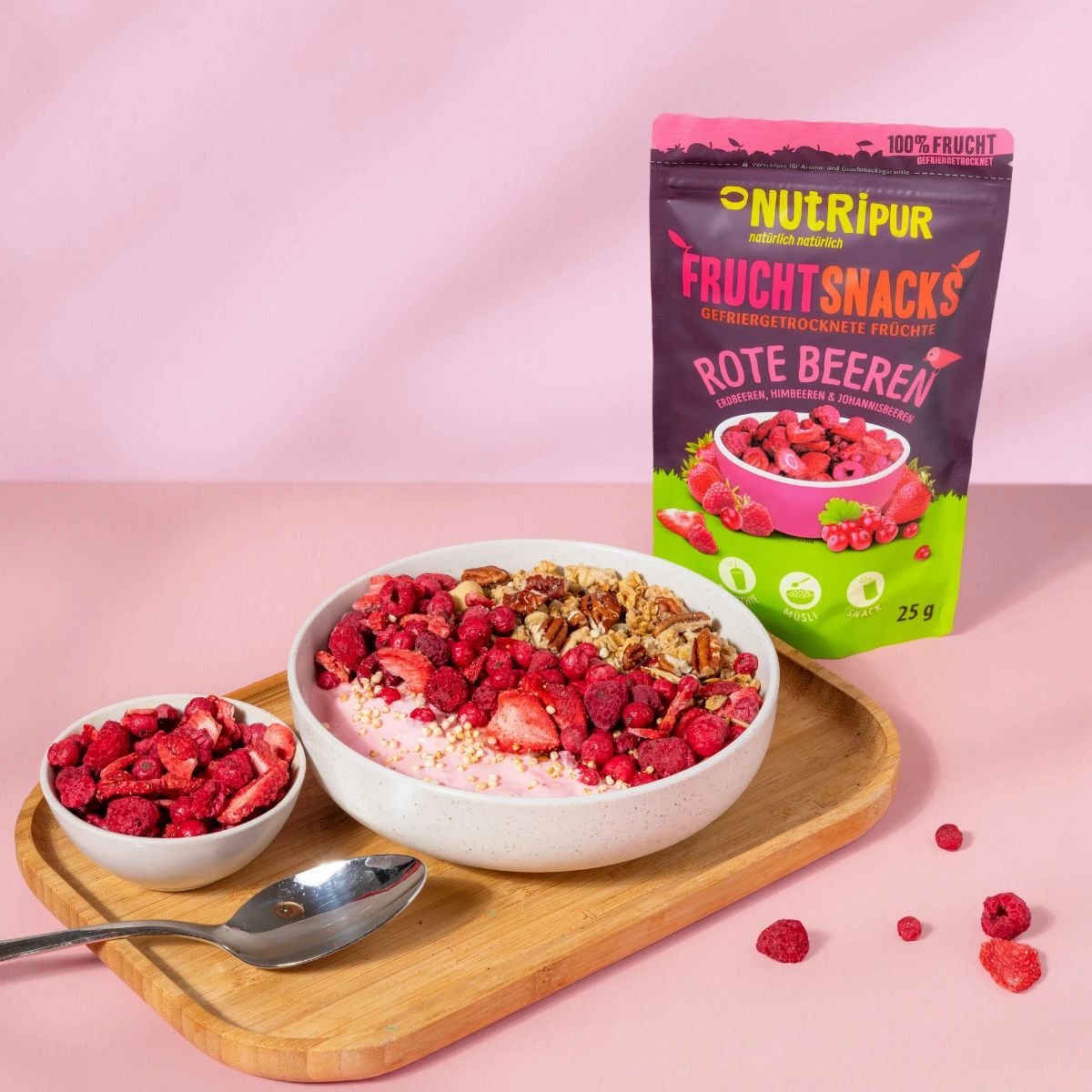 Schale mit Müsli und gefriergetrockneten Früchten. Daneben eine Schale mit Früchten und ein Beutel. 25g.