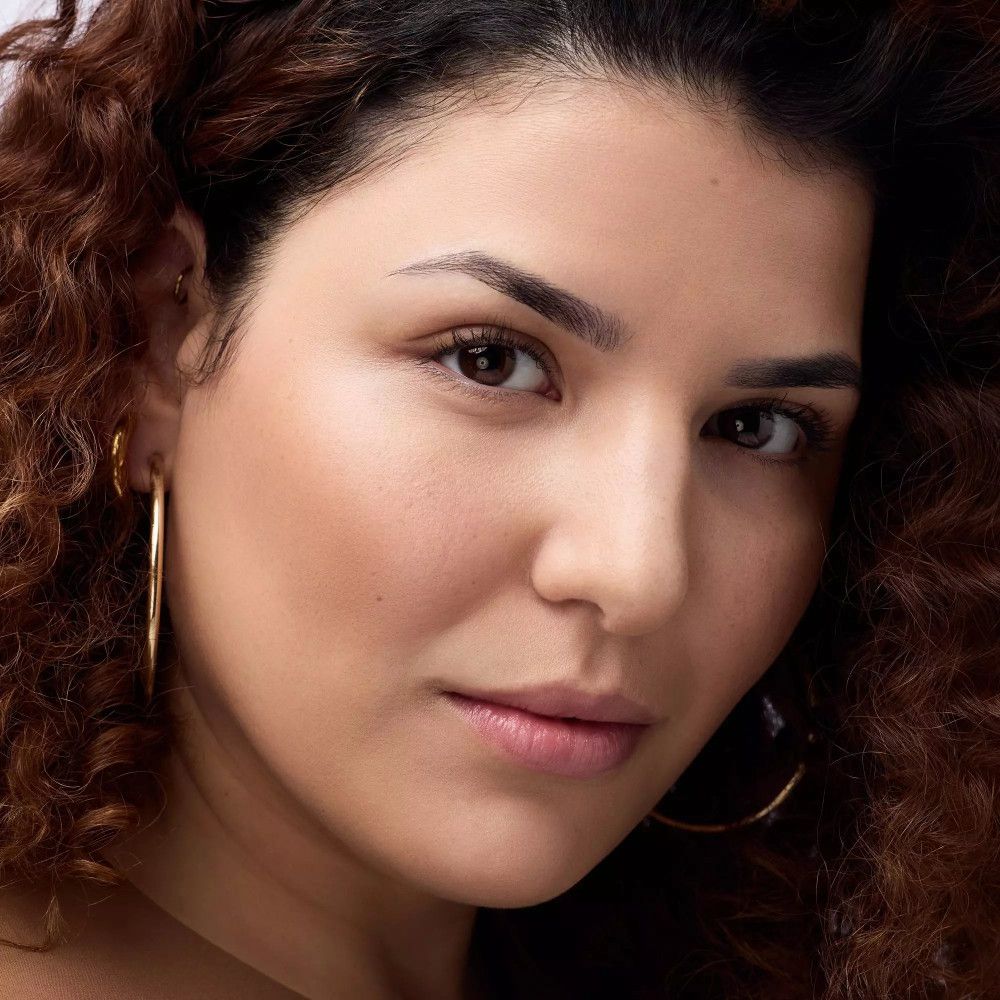 Porträt einer Frau mit Locken und Bronzer auf der Haut. Goldene Creolen.